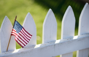 A small American flag sitting on a white picket fence post